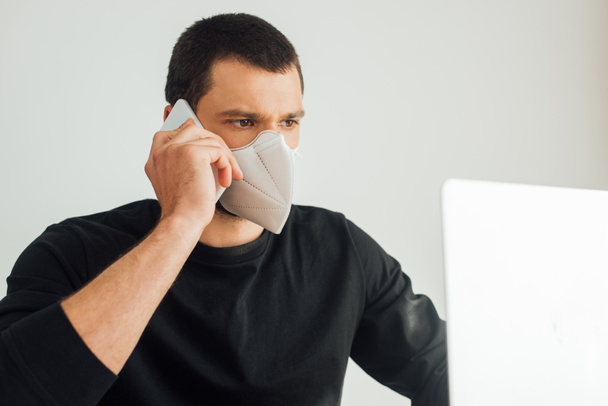 selective focus of freelancer in medical mask talking on smartphone near laptop  - Foto, immagini