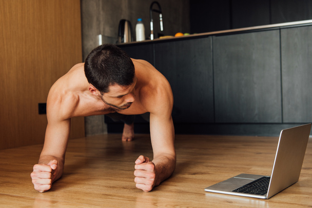 bearded and muscular man doing plank exercise while watching online training on laptop  - Фото, изображение