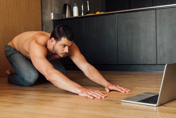 μυώδης άνθρωπος που κάνει άσκηση balasana, ενώ παρακολουθείτε online γιόγκα κατάρτισης στο laptop  - Φωτογραφία, εικόνα