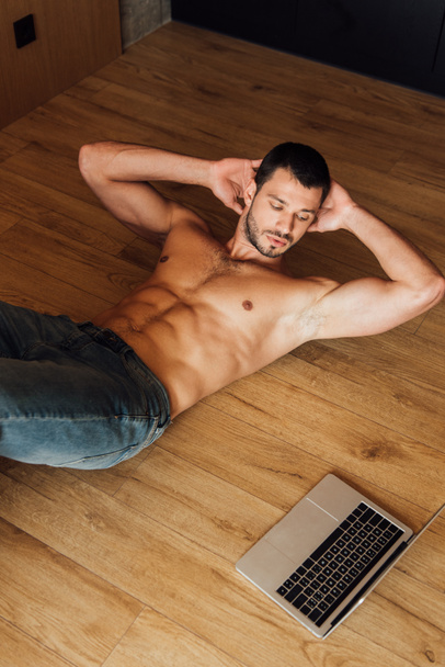 vista superior del hombre musculoso haciendo ejercicio mientras ve el entrenamiento en línea en el ordenador portátil
  - Foto, imagen