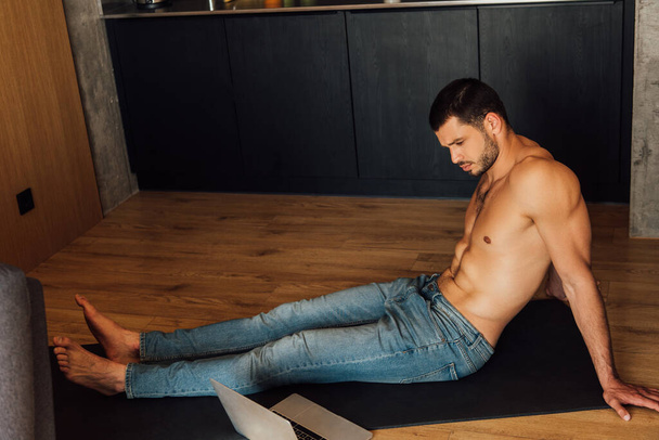 shirtless man sitting on yoga mat and watching online yoga training on laptop  - Фото, зображення