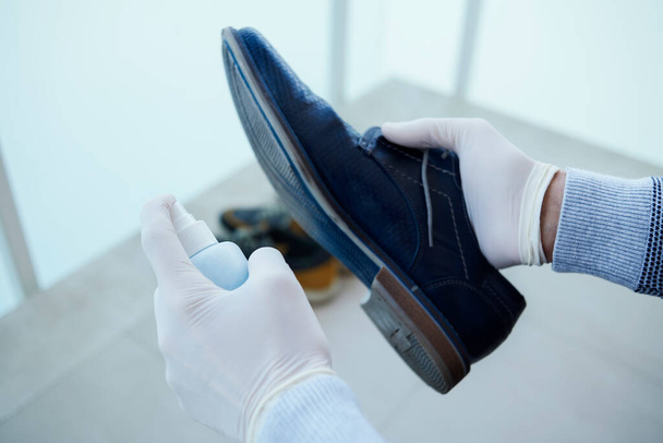 közelkép egy férfiról, gumikesztyűt visel, fertőtleníti a cipője talpát egy kék fertőtlenítőszerrel egy üvegből. - Fotó, kép