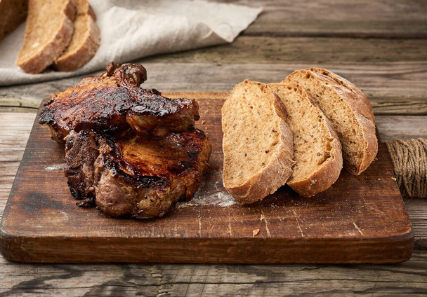 filetes de cerdo a la parrilla en el hueso en una tabla de cortar cocina, pan de harina de centeno en rodajas al horno vista superior
 - Foto, Imagen