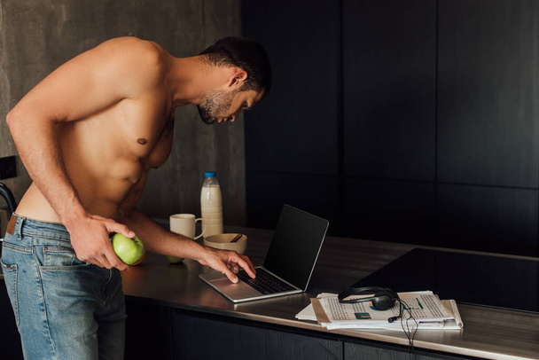 muscular freelancer holding apple and using laptop with blank screen  - Foto, Bild