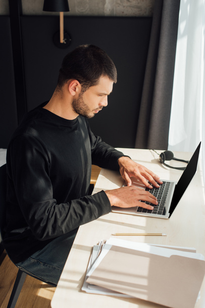 bearded freelancer using laptop near folder at home  - Photo, Image