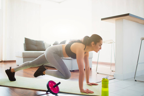 Jonge vrouw doet sport training in de kamer tijdens quarantaine. Oefenen in de ruimte op yoga mat. Stand in plank positie en het doen van mount klimmer oefening. - Foto, afbeelding