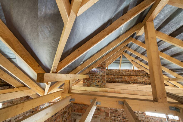 Podkroví budovy ve výstavbě s dřevěnými trámy střešní konstrukce a cihlových stěn. - Fotografie, Obrázek