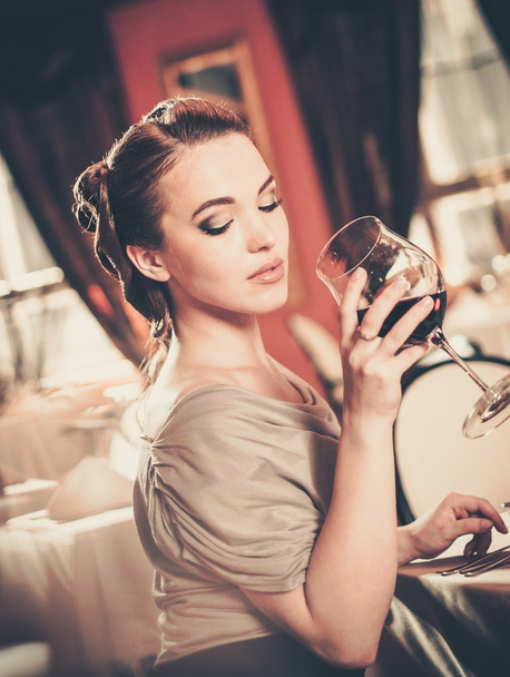 Beautiful young girl with glass of red wine alone in a restaurant - Photo, Image