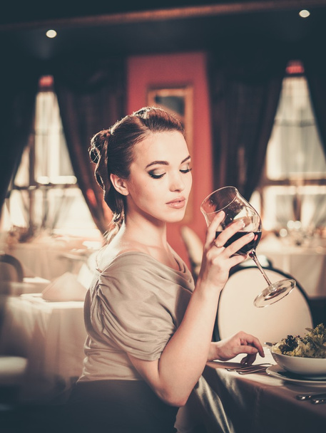 Beautiful young girl with glass of red wine alone in a restaurant - Fotografie, Obrázek