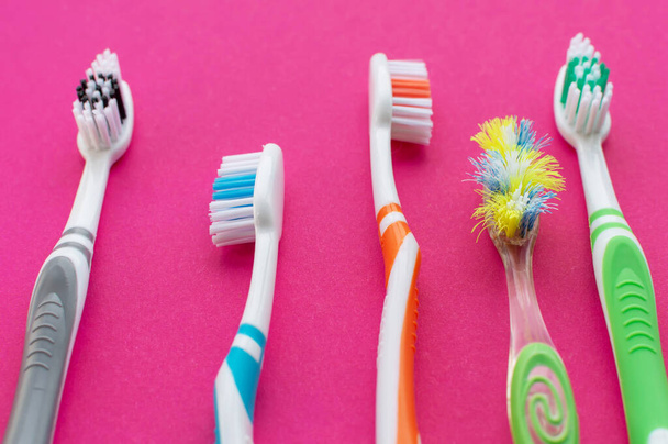 Multicolored new toothbrushes and an old toothbrush on a pink background. Close up.The concept of dental health. - Foto, Imagem