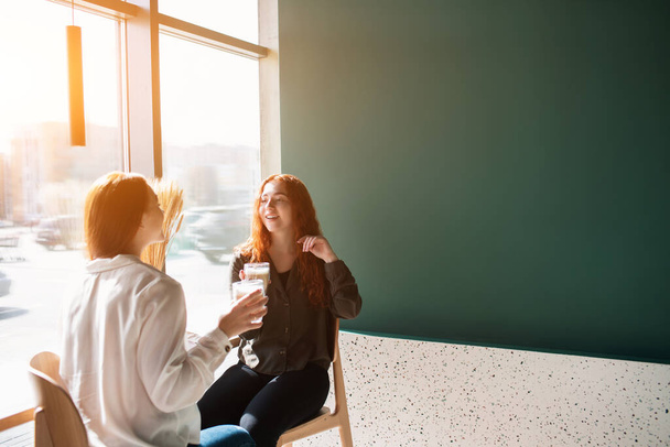 Młode kobiety rozmawiające w kawiarni. Modelki pijące kawę i śmiejące się. - Zdjęcie, obraz