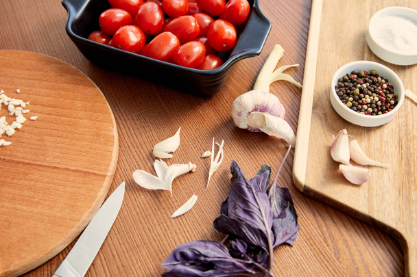 Vista de alto ángulo del recipiente con tomates, cuchillo y tablas de cortar con ingredientes sobre fondo de madera
 - Foto, Imagen