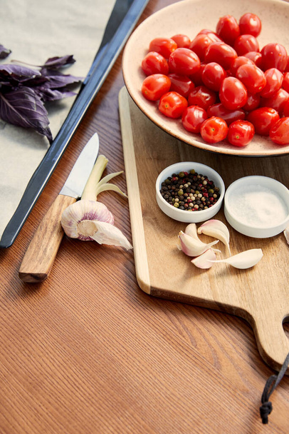 High angle view of oven tray, plate and cutting board with ingredients near knife on wooden background - Foto, afbeelding