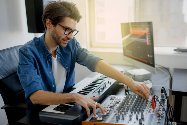 music producer is composing a song on synthesizer keyboard and computer in recording studio. Man is working on sound mixer in recording studio or DJ is working in broadcasting studio - Foto, imagen
