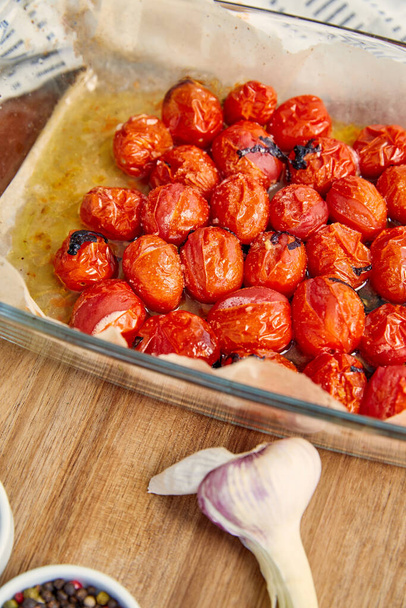 Vysoký úhel pohledu připravených rajčat v misce na pečení u česneku na dřevěném pozadí - Fotografie, Obrázek