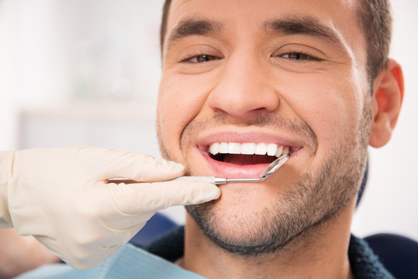knappe lachende man bij het doen van checkup op van tandarts chirurgie - Foto, afbeelding