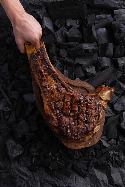 filete de tomahawk a la parrilla en un plato de madera listo para comer. Sobre el carbón de fondo
 - Foto, imagen