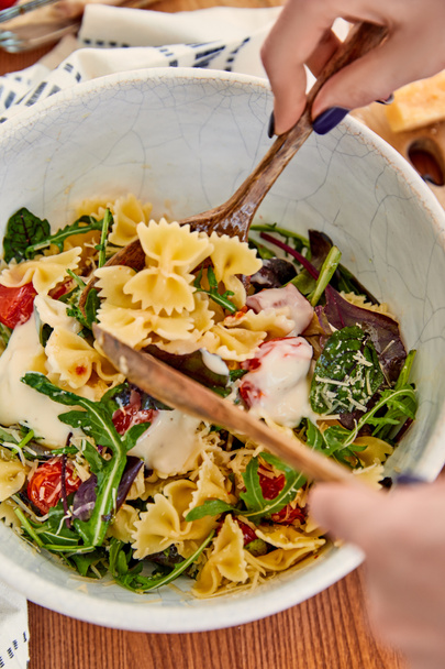 Cropped view of woman mixing pasta salad with mayonnaise in bowl near napkin on wooden background - Foto, afbeelding