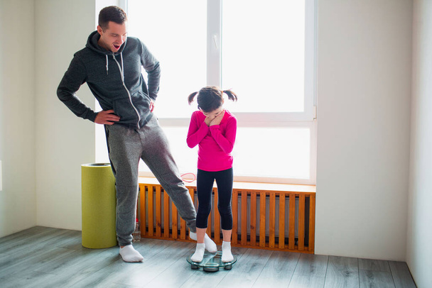 Slimming. Father and daughter are weighed on indoor household scales. Funny and joyful moments having fun in the family. Diet, proper nutrition and healthy lifestyle concept. - Фото, зображення