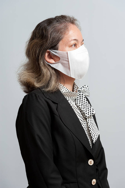 Retrato de medio cuerpo de una mujer de raza mixta de mediana edad vestida con una máscara facial 3D desechable blanca para protegerse contra el nuevo coronavirus (COVID-19). Aislado sobre fondo blanco. Vista lateral
. - Foto, imagen
