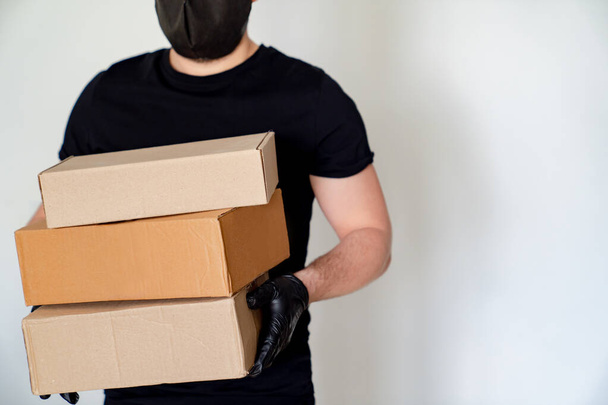 Delivery man in black hold cardboard boxes - Фото, зображення