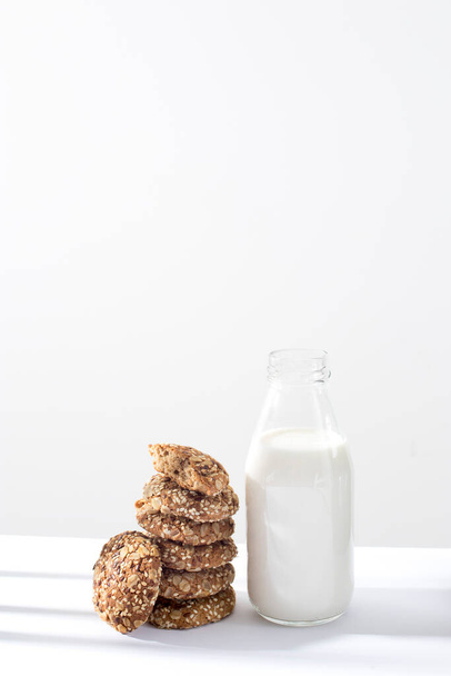 Mutfaktaki gri bir duvara karşı üzerinde susam tohumu ve badem serpiştirilmiş yulaf ezmeli açık bir süt şişesi. Boşluğu kopyala - Fotoğraf, Görsel