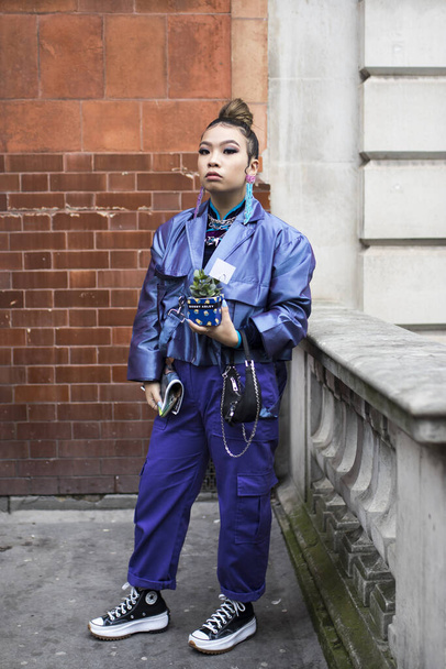 London, UK - 15 January, 2020, Girl with a ponytail in a blue silk shiny jacket and trousers with pockets, jewelry with a succulent in a pot posing. Fashionable people on the street . Street style. - 写真・画像