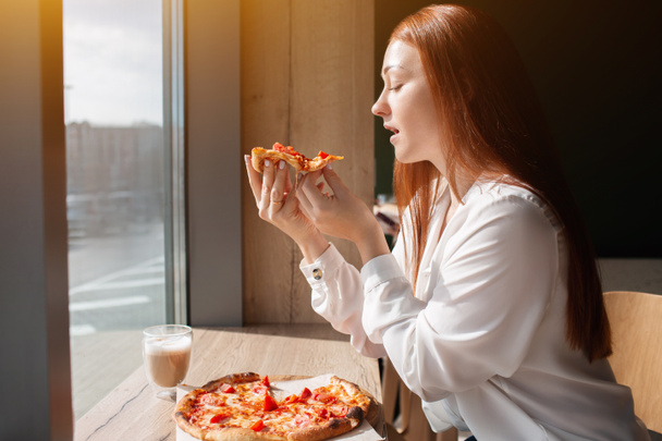 женщина-модель держит кусок пиццы в руках. молодая женщина ест пиццу в кафе
. - Фото, изображение
