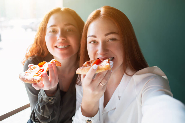 Modelki robią sobie selfie przez telefon w kawiarni. Młode kobiety uśmiechające się i jedzące pizzę - Zdjęcie, obraz