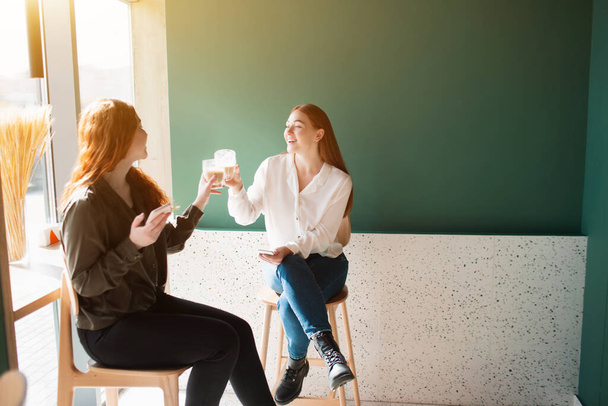 Las modelos femeninas beben café en un café. Las mujeres jóvenes hablan y sonríen
 - Foto, imagen