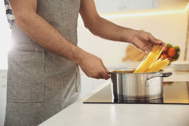 Man cooking pasta on stove in kitchen, closeup - Foto, imagen