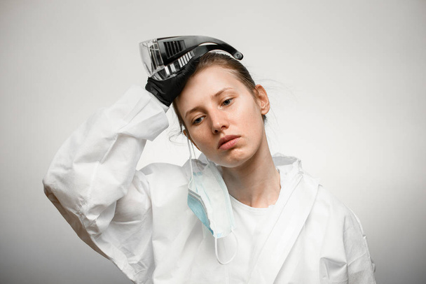 mladá unavená žena lékař v ochranném lékařském oděvu sundal brýle - Fotografie, Obrázek