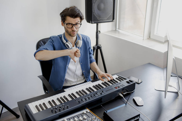 thumbs down. Composer hands on piano keys in recording studio. music production technology, man is working on pianino and computer keyboard. Bad employee and specialist. Frustrated and Unprofessional. - Foto, afbeelding