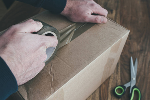 close-up of person sealing up shipping box with parcel tape - Zdjęcie, obraz