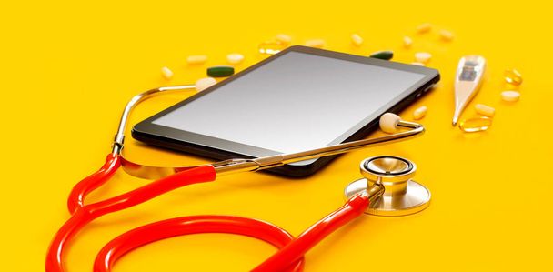Piros sztetoszkóp és egy tabletta PC orvosi alkalmazással, másolás Elszigetelt sárga háttér. Koncepció telemedicina, mock up, felső nézet, tabletták, gyógyszer, hőmérő, orvos online - Fotó, kép