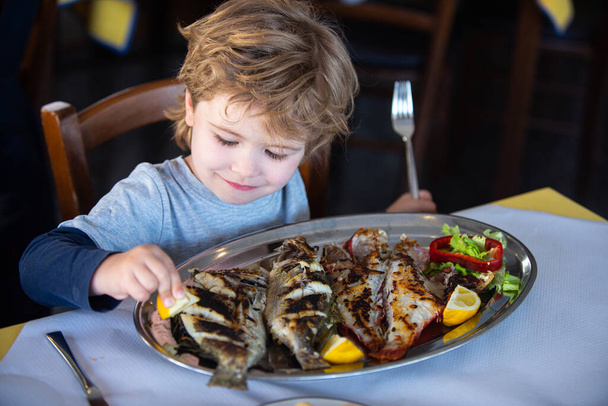 Fish for food. Child wuth lemon and fish plate meal. Dinner in sea restaurant. Seafood with iodine for a healthy diet eating. - Photo, Image