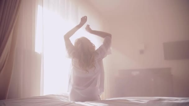soft light. girl blonde woke up in the morning pulls up her hands. on bed in bedroom on sunny weather window background. sunlight shines into the room. Sitting wakes up - Video