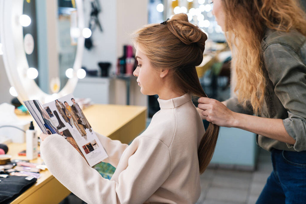 Image of a pretty young beautiful woman client with hair stylist in saloon reading magazine. - Fotoğraf, Görsel