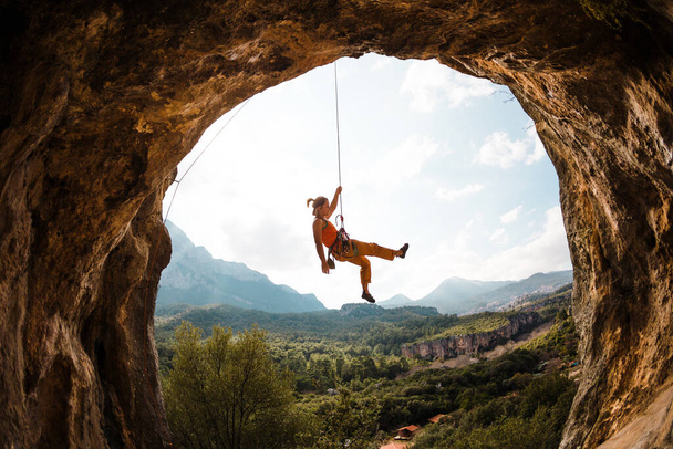 Escalador colgando de una cuerda. Una mujer trepa una roca en forma de arco. La chica sube a la cueva. Cuerda de trepar para el trenzado. Escalada en roca en Turquía . - Foto, imagen
