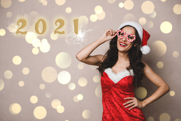 Beautiful woman in Christmas costume with party glasses on beige background. Bokeh effect - Фото, изображение