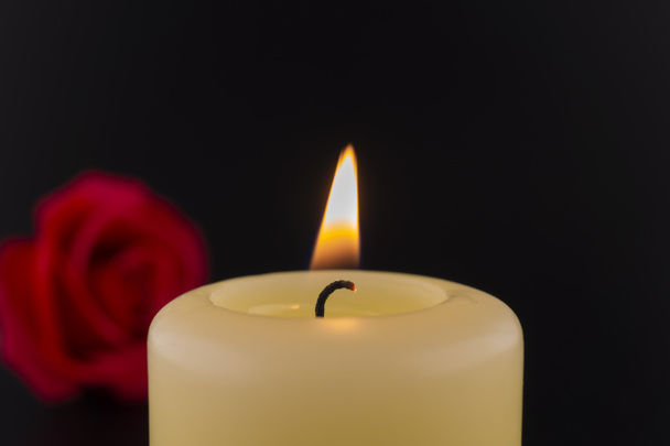 Jedna hořící žlutá svíčka vedle červené růže na tmavém pozadí - Fotografie, Obrázek