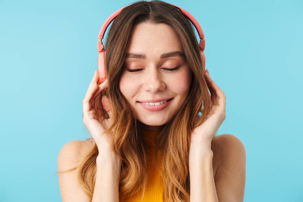 Portrait of beautiful joyous woman wearing headphones listening to music isolated over blue background in studio - Foto, Imagem