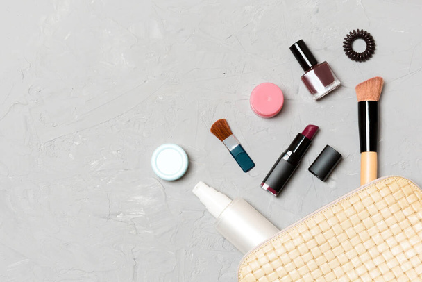 Top view of make up products fallen out of cosmetics bag on cement background. Cosmetic concept with space for your design. - Photo, Image