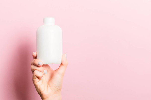 Close-up van vrouwelijke hand houden cosmetica fles op roze achtergrond met kopieerruimte. - Foto, afbeelding