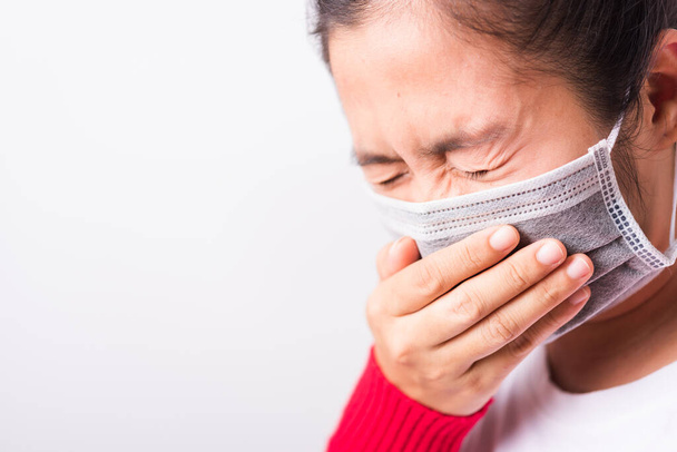 Closeup Asian adult woman wearing red shirt and face mask protective against coronavirus or COVID-19 virus or filter dust, air pollution her sneezing use hand close mouth, isolated white background - Fotó, kép