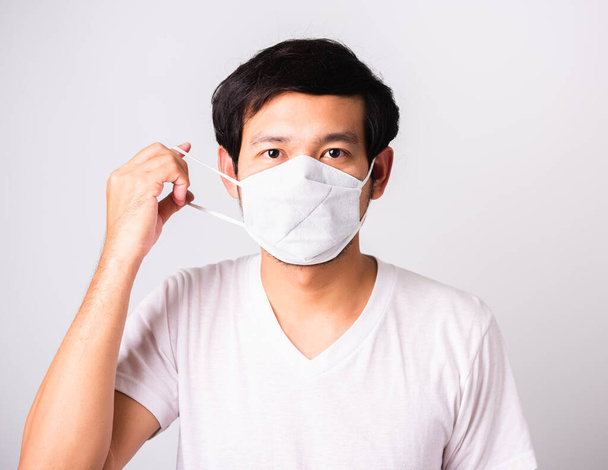 Closeup Asian handsome Man wearing surgical hygienic protective cloth face mask against coronavirus, studio shot isolated white background, COVID-19 medical concept - Foto, afbeelding