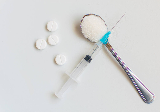 A spoon of sugar, a syringe and pills on a white background. The concept of harm to sugar and the onset of diabetes. - Foto, Imagen
