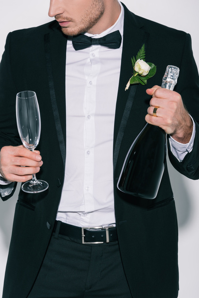 cropped view of bridegroom holding champagne glass and bottle on white background - Foto, imagen