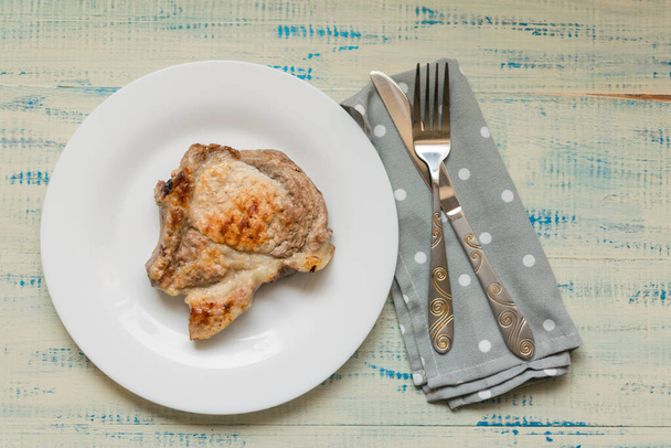A piece of fried meat on a white plate on a light wooden background. - Valokuva, kuva
