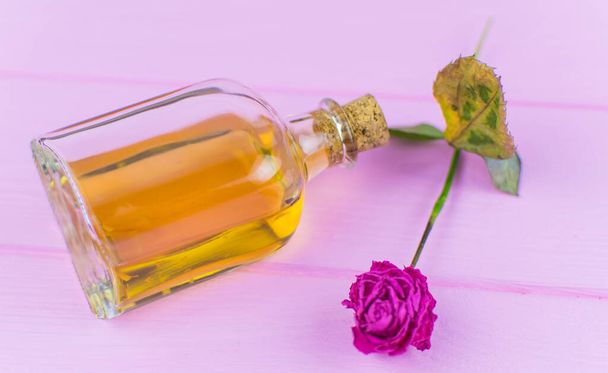 A bottle with a yellow elixir on a pink wooden background. - Foto, Imagen